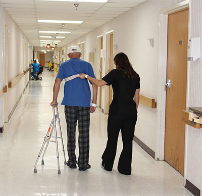 A female nurse is assisting a male patient to walk down the hospital hall with a gait belt