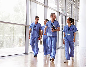 Four healthcare workers in scrubs walking in corridor