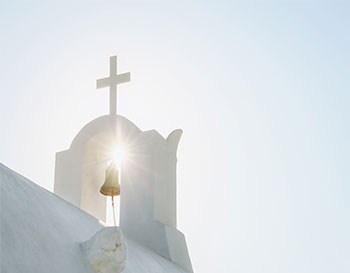 White Orthodox Church belfry with cross and bell in sunshine on sky background. Santorini island, Greece