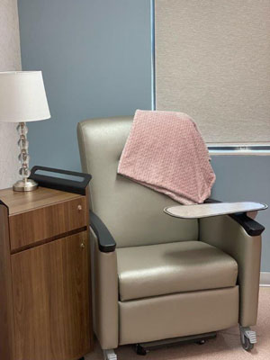 Picture of an outpatient infusion therapy room with a side table, recliner, monitor, and window.